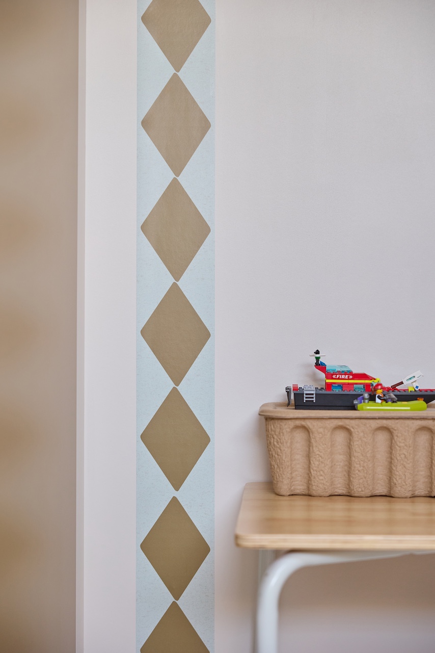 Behangrand met ruitpatroon als verticaal accent naast een kast in een rustige kinderkamer.